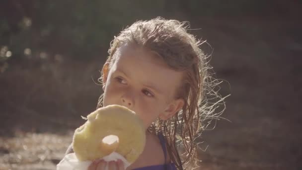 Bella Bambina Mangiare Una Grande Ciambella Sulla Spiaggia — Video Stock