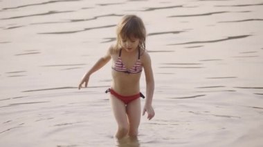 Bikini giyen sevimli küçük kız sığ sularda oynuyor, ağır çekimde.