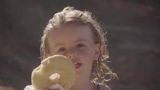 Mooi Klein Meisje Eten Een Grote Donut Het Strand — Stockvideo