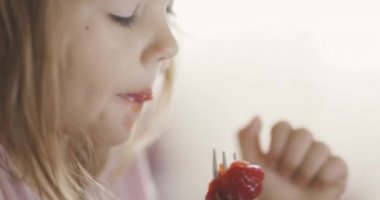 Küçük şirin bir kızın oturma odasında çilek yiyip tablet izlemesi, seçici bir odak noktası. 