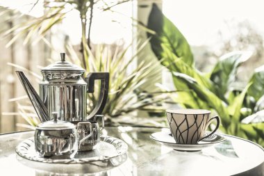 Sabah güneşinde sıcak çaydanlığı tutan kadınlar, retro renkler, güneşin parladığı bir pencere.