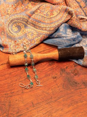 Gümüş renkli yeşil akik boncuklu bilezik, üzerinde Hint sapı ve ahşap masa arkasında ahşap grev var.