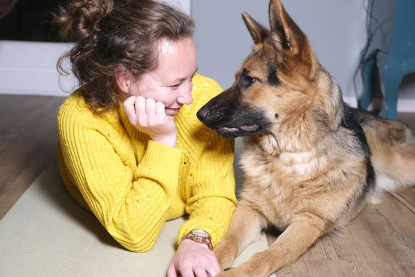 Genç bir kadın, Alman çoban köpeğiyle yerde uzanıyor ve odada dinleniyor.
