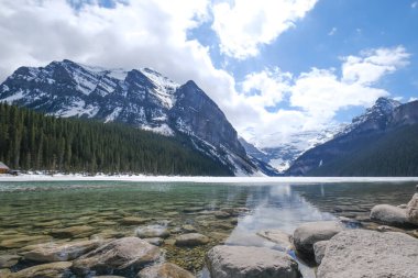 Fairview Dağı, kısmen donmuş göl, ön planda kayalar. Louise Gölü Ulusal Parkı, Alberta Kanada