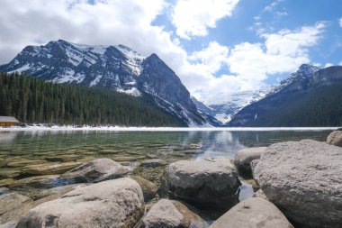 Fairview Dağı, kısmen donmuş göl, ön planda kayalar. Louise Gölü Ulusal Parkı, Alberta Kanada