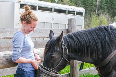 Genç bir kadın Banff Ulusal Parkı 'nda atları besliyor.