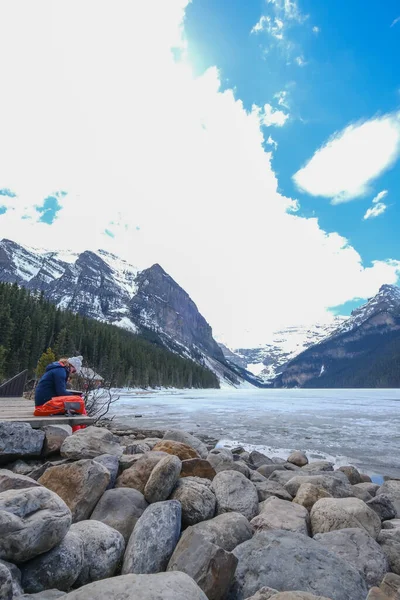 Louise gölünün kıyısında oturan bir kadın, kitap okuyor, kamera çantası hemen yanında, Kanada Kayalıkları, Kanada