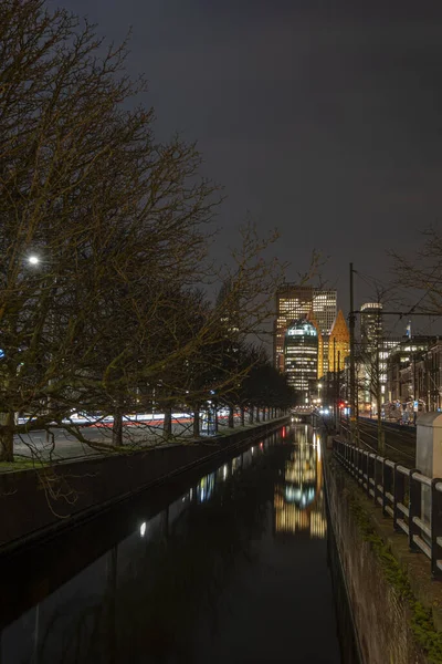 The Hague, the Netherlands - 18 February 2019: Skyline of The Hague at night with canal in front and high buildings , Castalia, Helicon, Zurichtoren and the Muzentoren in background — стокове фото