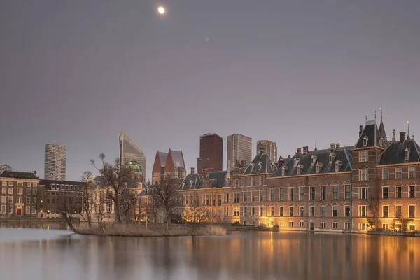Hága - 2019. február 17.: Hága, Neherland. Binnenhof kastély, holland parlament, a bírósági tó, hátterében felhőkarcolók, kék ég a hold, szürkület, kék óra — Stock Fotó