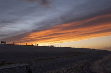 Hollanda 'da günbatımında mavi, morumsu, turuncu, mor ve sarı renkli güzel bulutlu gökyüzü, sonbahar, gökyüzüne karşı bir kadın silueti