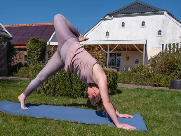 Mujer joven haciendo ejercicios de yoga en el jardín en casa, pose cosa salvaje — Foto de Stock