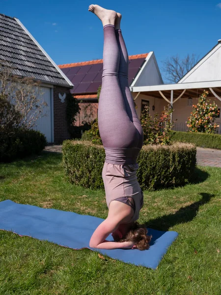 Mujer joven haciendo ejercicios de yoga en el jardín en casa. posada de cabeza — Foto de Stock