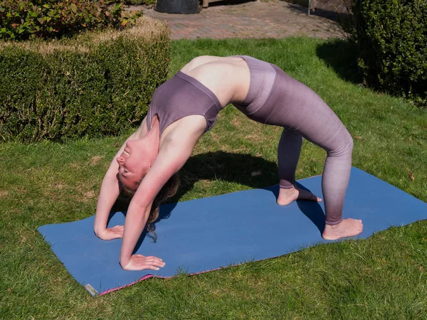 Mujer joven haciendo ejercicios de yoga en el jardín en casa en plena pose puente — Foto de Stock