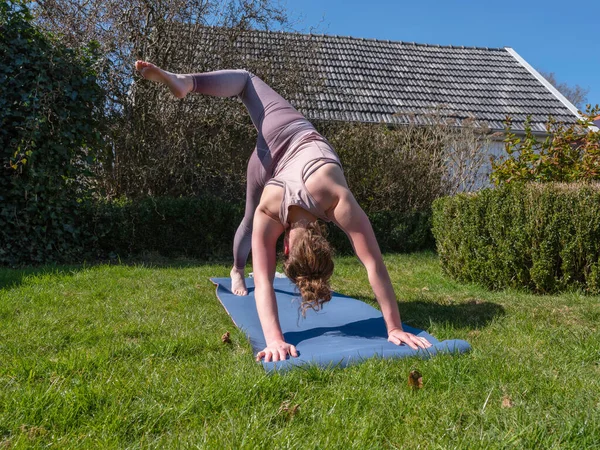 Mujer joven haciendo ejercicios de yoga en el jardín en casa, pose cosa salvaje — Foto de Stock