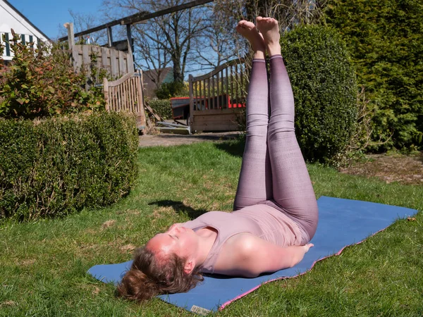 Mujer joven haciendo ejercicios de yoga en el jardín en casa en la pierna plantea — Foto de Stock