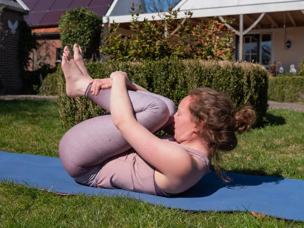 Mujer joven haciendo ejercicios de yoga en el jardín en casa, en pose liberadora de aire — Foto de Stock