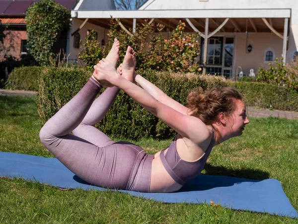 Mujer joven haciendo ejercicios de yoga en el jardín en casa en pose de arco — Foto de Stock