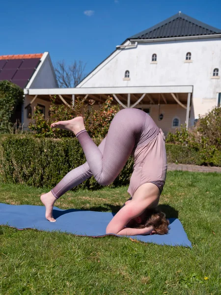 Mujer joven haciendo ejercicios de yoga en el jardín en casa. posada de cabeza — Foto de Stock