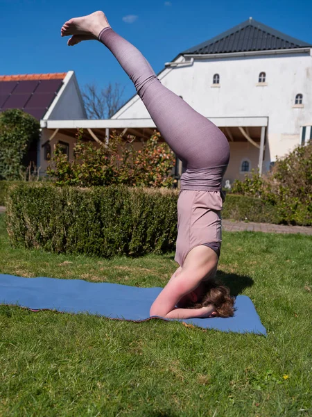 Mujer joven haciendo ejercicios de yoga en el jardín en casa. posada de cabeza — Foto de Stock