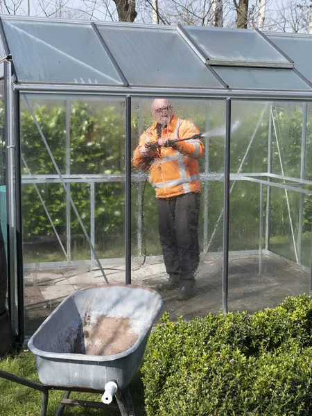 Construction worker cleaning filth with high pressure cleaner from a glass greenhouse