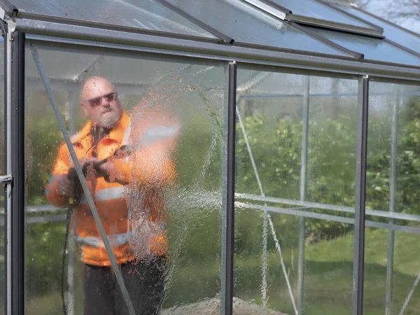 Работник строительства очищает грязь очистителем высокого давления от стеклянной теплицы — стоковое фото