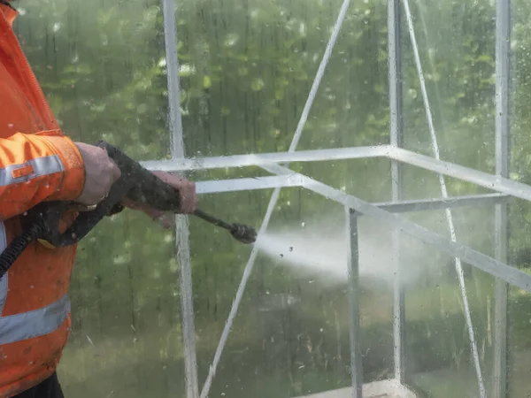 Construction worker cleaning filth with high pressure cleaner from a glass greenhouse