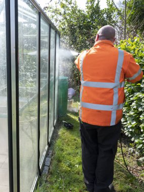 Construction worker cleaning filth with high pressure cleaner from a glass greenhouse clipart