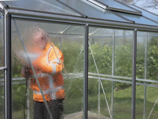 Работник строительства очищает грязь очистителем высокого давления от стеклянной теплицы — стоковое фото
