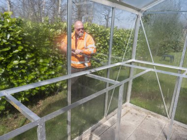 İnşaat işçisi cam bir seradan yüksek basınçlı temizleyici ile pisliği temizliyor.