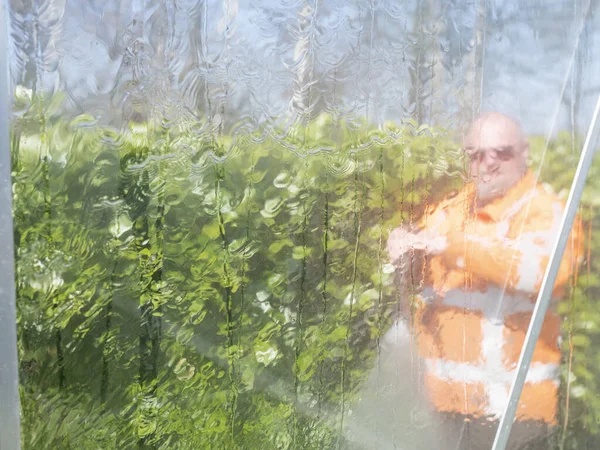 Construction worker cleaning filth with high pressure cleaner from a glass greenhouse