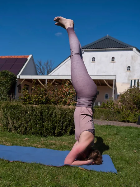 Mujer joven haciendo ejercicios de yoga en el jardín en casa. posada de cabeza — Foto de Stock