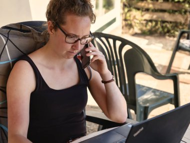 Kadın evde bilgisayarla, akıllı telefonla ve bahçede defter ile çalışıyor, tecrit sırasında, konsept: