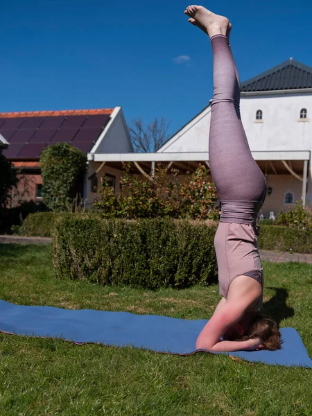 Mujer joven haciendo ejercicios de yoga en el jardín en casa. posada de cabeza — Foto de Stock