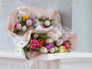 İki buket çiçek açan lalenin yakın görüntüsü yeşil duvarlı beyaz şömine rafında yatıyor.