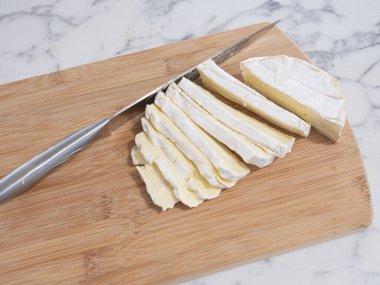 Taze dilimlenmiş Brie peyniri, tahta kesme tahtasının üzerinde bıçak, yüzey, mermer tezgah.