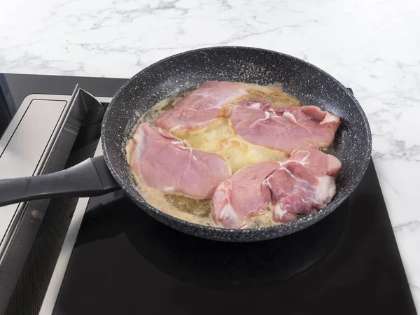 frying pan on an induction plate in which pork chops are baking