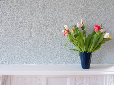 Yeşil arkaplanda mavi bir vazoda bulunan laleler.