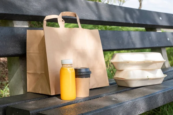Lunch in nature, paper bag with sandwiches, coffee tea and orange juice are in front of the bag on the picnic bench. Recycling and environmentally friendly product concept. Take away food.