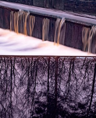 Weir 'da çok fazla su birikinti boyunca akar, sudaki ağaçların yansıması, uzun süre maruz kalan su hareketi. Konum: Friesland, Hollanda.