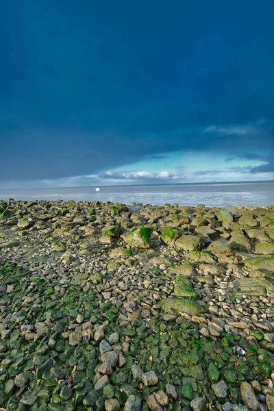 A container ship has lost a cargo at sea, off the coast of Friesland, the Netherlands. A freezer floats at sea, environmental pollution, rocks in foreground. Unesco world heritage.