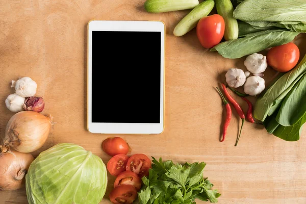 Top view of Fresh vegetables with tablet touch computer gadget on wooden table background.