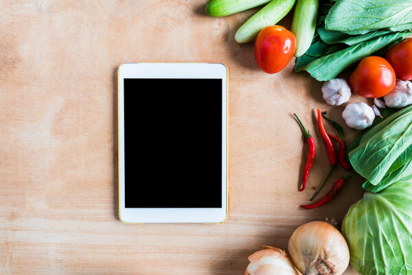 Top view of Fresh vegetables with tablet touch computer gadget on wooden table background.