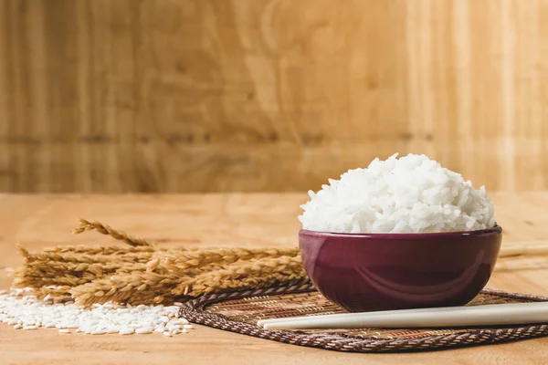 Riz cuit dans un bol avec grain de riz cru et plante de riz sec sur fond de table en bois . — Photo