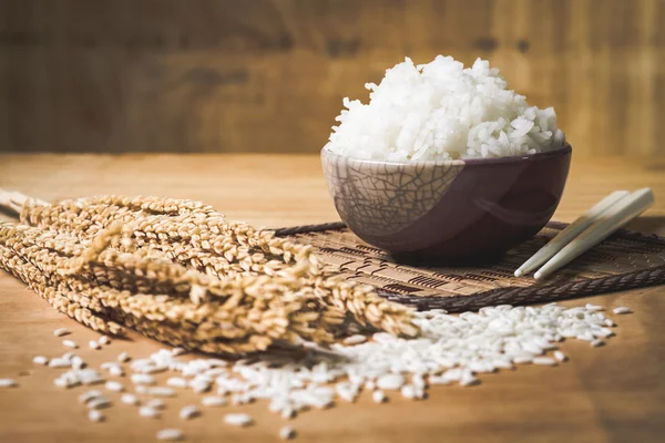 Riz cuit dans un bol avec grain de riz cru et plante de riz sec sur fond de table en bois . — Photo