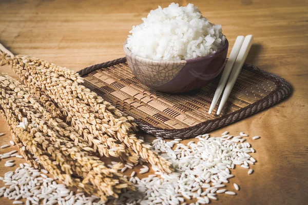 Riz cuit dans un bol avec grain de riz cru et plante de riz sec sur fond de table en bois . — Photo