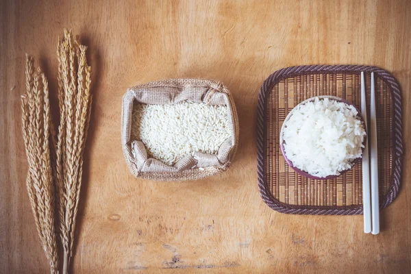 木製のテーブルの背景に生米粒と乾燥米植物とボウルで炊いた米. — ストック写真