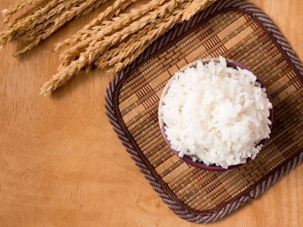 Cooked rice in bowl with dry rice plant on  wooden table background.