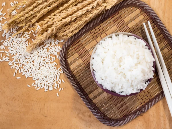 Arroz cozido em tigela com grão de arroz cru e planta de arroz seco sobre fundo de mesa de madeira . — Fotografia de Stock