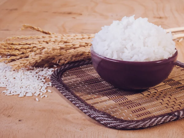 Riz cuit dans un bol avec grain de riz cru et plante de riz sec sur fond de table en bois . — Photo