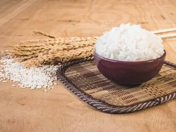 Riz cuit dans un bol avec grain de riz cru et plante de riz sec sur fond de table en bois . — Photo
